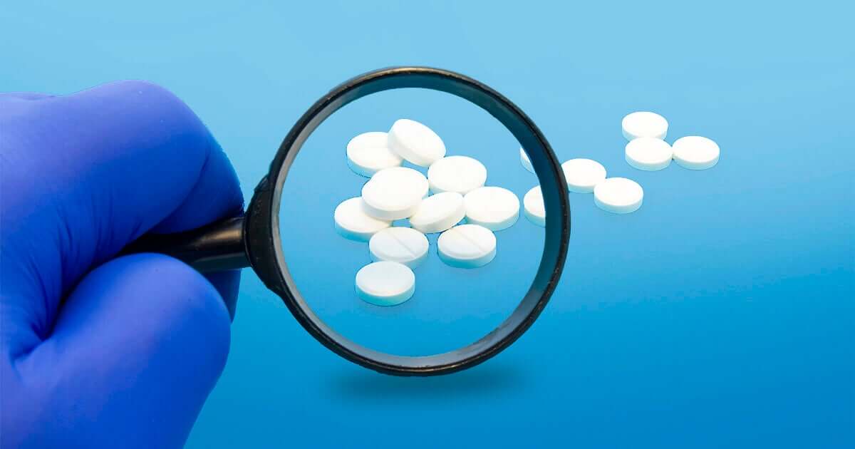 Magnify glass and gloved hand looking at white pills