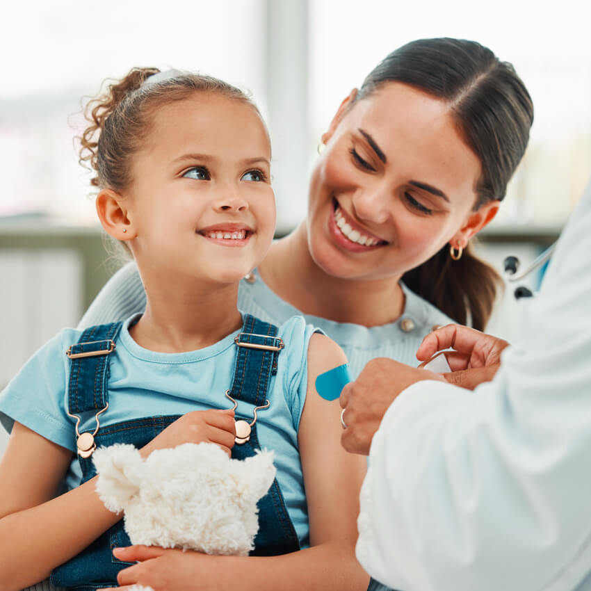 A mother with her young daughter at a doctor's appointment. Girl just received a shot, but is smiling.